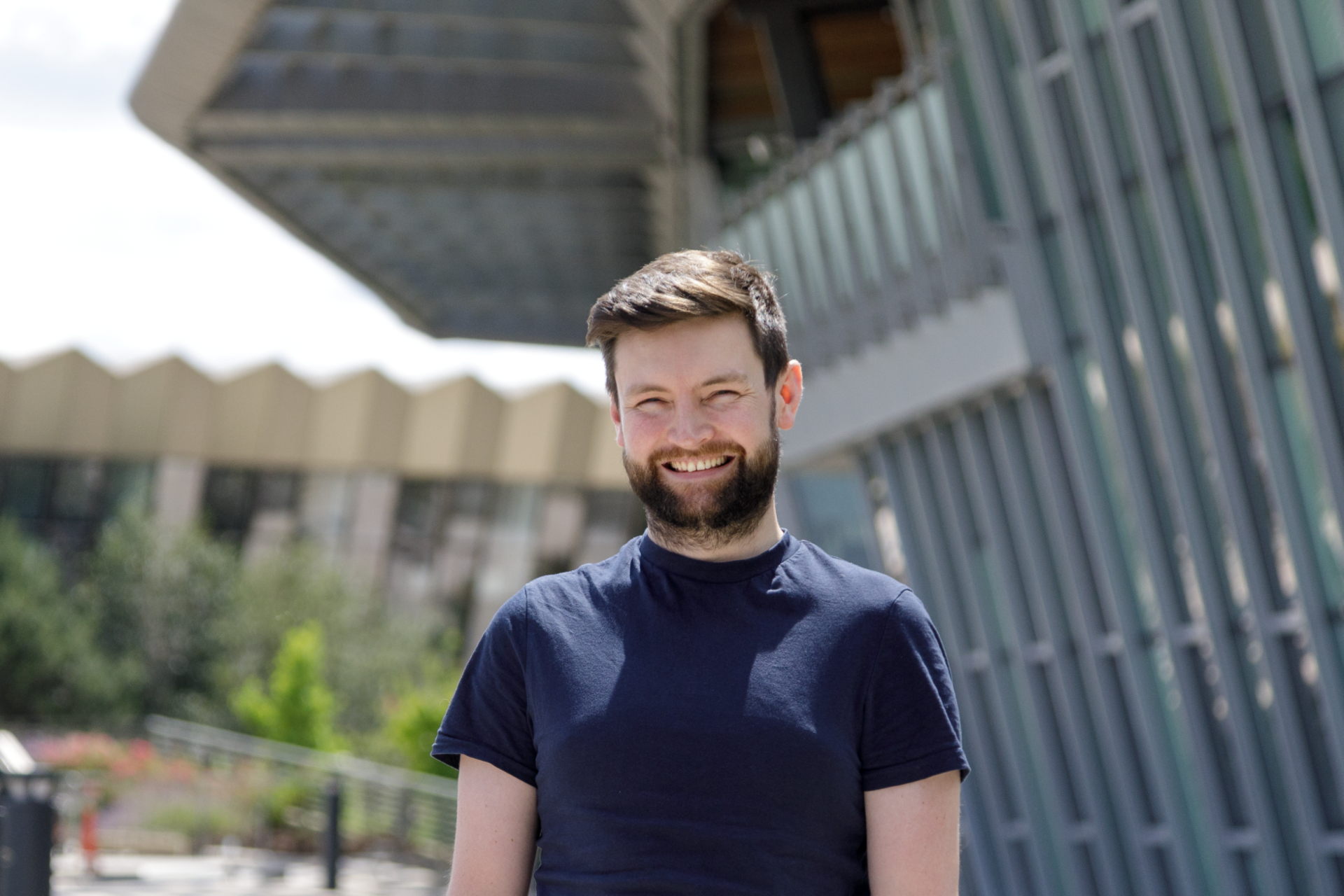 A picture of George smiling, he is standing in the grounds of the Wellcome Genome Campus.