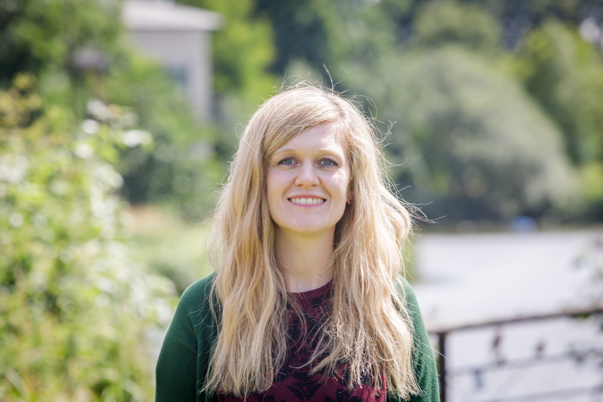 A picture of Katie smiling in front of a lot of trees that are blurred in the background. Katie is a Postdoctoral Research Scientist (Ecology) at Wellcome Sanger Institute