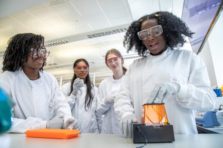 4 students wearing labcoats looking excited during science experiment.